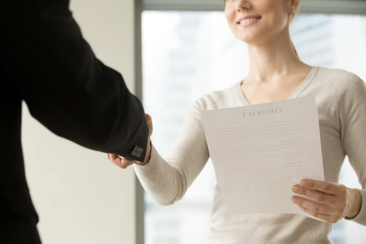 woman holding contract shaking hands with person in blazer